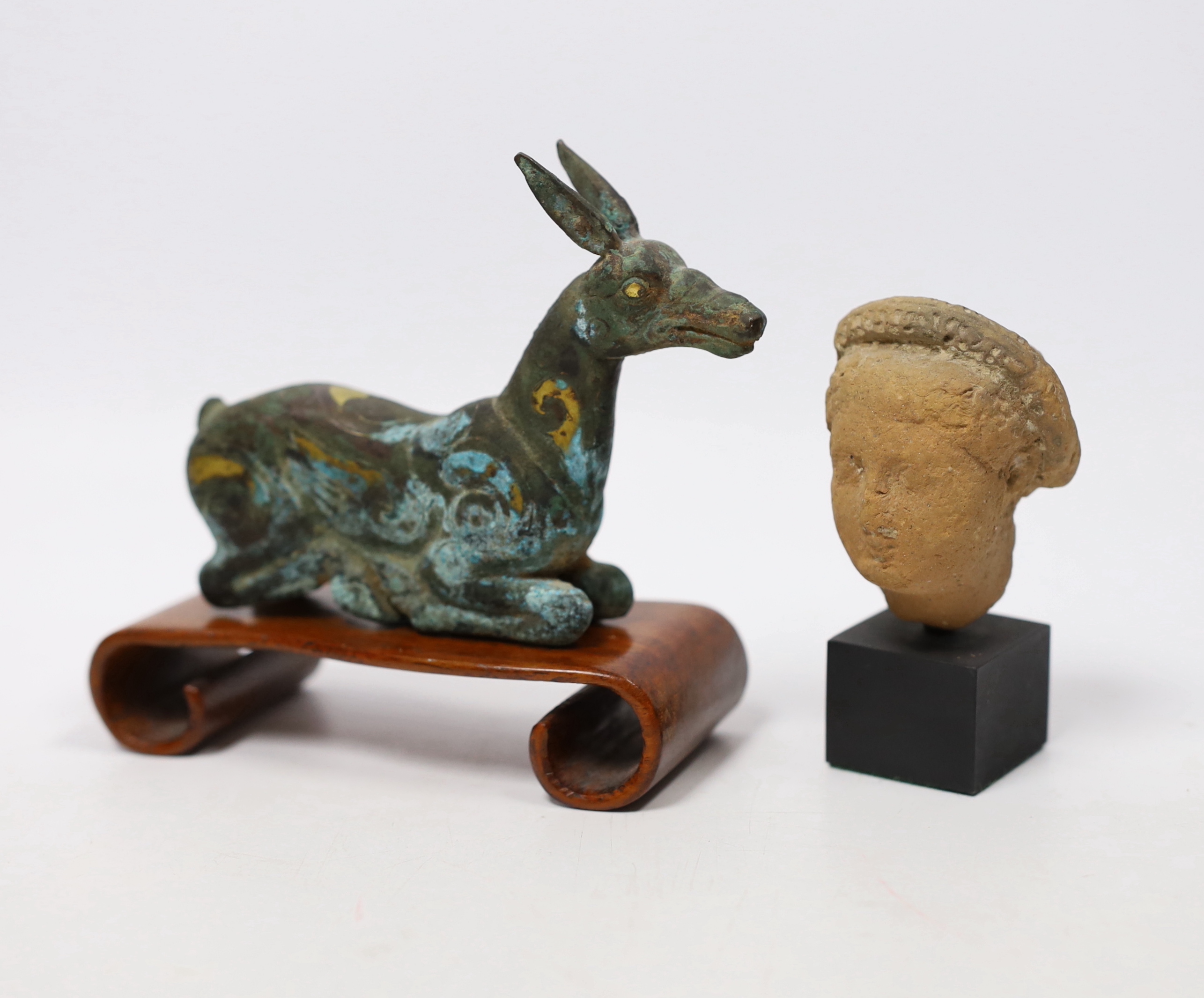 A Chinese bronze and parcel gilt Han style figure of a seated deer, and a small Etruscan terracotta head on stand